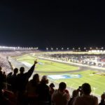 The Coca Cola 600 night race at Charlotte Motor Speedway with fans cheering from the grandstands.