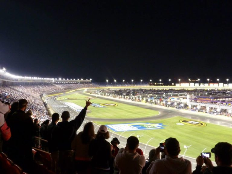 Night race at Charlotte Motor Speedway with fans cheering from the grandstands.
