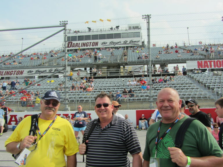 Three race fans pose on the frontstretch at Darlington Raceway before the Southern 500, enjoying their Darlington NASCAR Packages weekend.