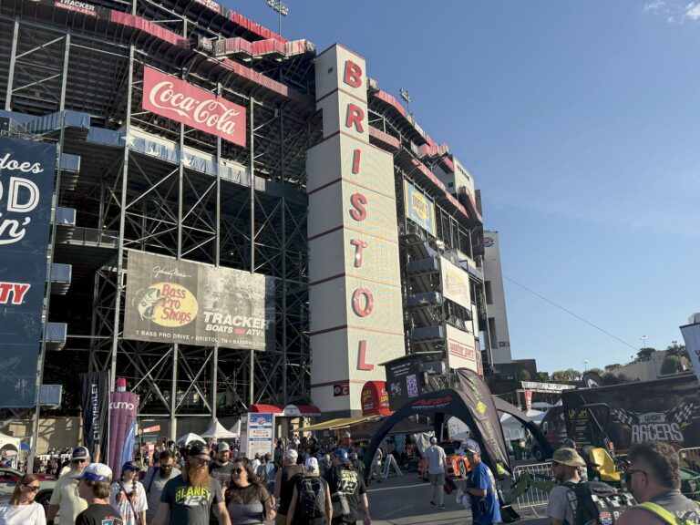 Fans gather outside the main entrance of Bristol Motor Speedway under clear blue skies on race day.