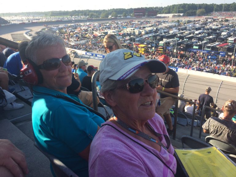 Two fans relax in the Darlington Raceway grandstands with a panoramic view of the infield, enjoying the Southern 500 with their Darlington NASCAR Tickets package.