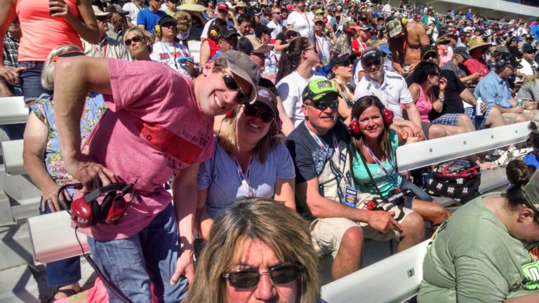 Group of guests enjoying Las Vegas NASCAR Packages in the grandstands at Las Vegas Motor Speedway under bright sunny skies.