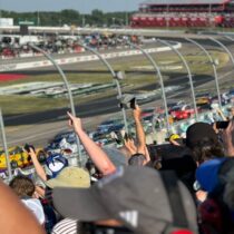 Fans cheer and wave as NASCAR Cup Series cars thunder past the grandstands at Iowa Speedway.