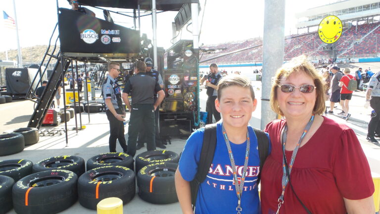 Two smiling NASCAR fans stand near pit road tires and team equipment at Phoenix Raceway.
