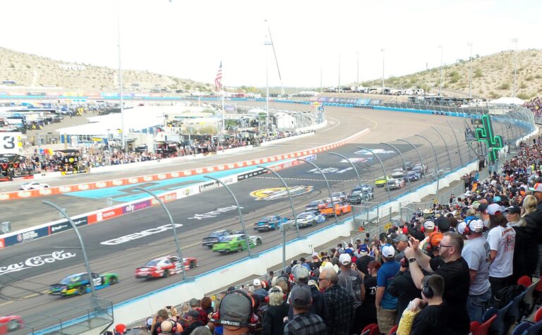 NASCAR Cup Series cars race past Phoenix NASCAR Ticket Package guests in the grandstands at Phoenix Raceway.