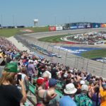 RaceAway Kansas NASCAR Ticket Package guests watch as NASCAR cars race around Kansas Speedway’s wide, high-banked turns.