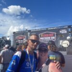 Fans pose in front of the Cook Out Southern 500 stage at Darlington Raceway, enjoying exclusive access included with Darlington NASCAR Ticket Packages.