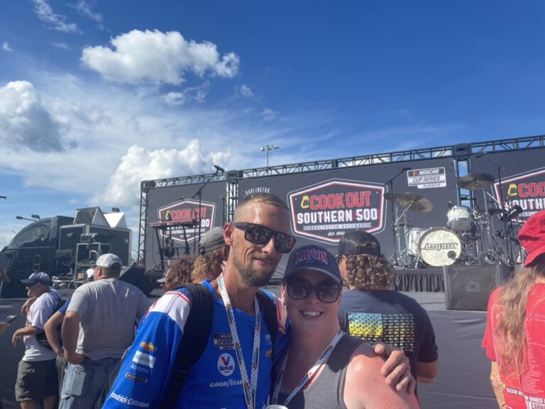 Fans pose in front of the Cook Out Southern 500 stage at Darlington Raceway, enjoying exclusive access included with Darlington NASCAR Ticket Packages.