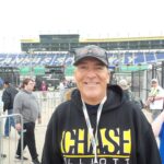 A smiling NASCAR fan wearing a Chase Elliott hoodie stands near the entrance of Kansas Speedway.