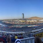 Panoramic view of Phoenix Raceway during a NASCAR race with desert mountains in the background.