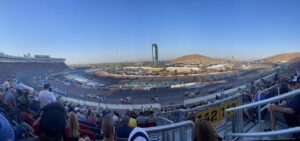 Panoramic view of Phoenix Raceway during a NASCAR race with desert mountains in the background.