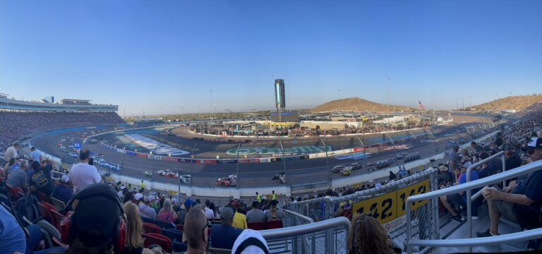 Panoramic view of Phoenix Raceway during a NASCAR race with desert mountains in the background.