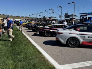 Race cars lined up on pit road at Kansas Speedway under a clear blue sky