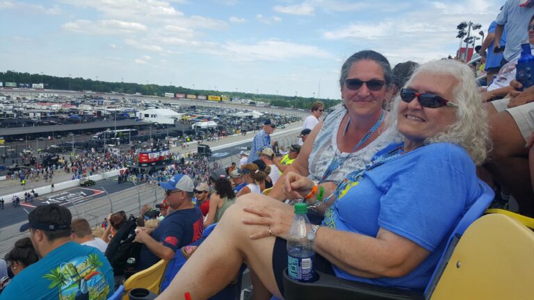 Two smiling fans relax in the Darlington Raceway grandstands overlooking pit road and the infield.