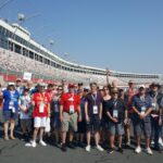 A group of RaceAway Hospitality Charlotte NASCAR Ticket Package guests standing on the track at Charlotte Motor Speedway with grandstands in the background.
