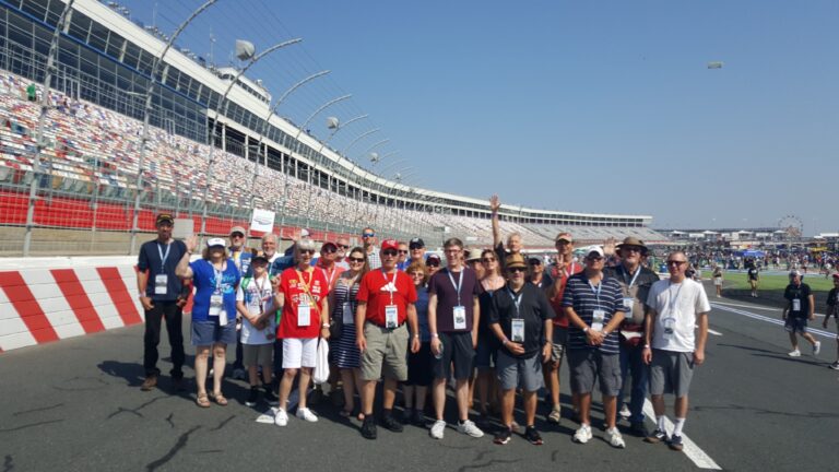 A group of RaceAway Hospitality guests standing on the track at Charlotte Motor Speedway with grandstands in the background.