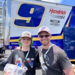Father and son smiling in front of the Hendrick Motorsports hauler at Iowa Speedway during their RaceAway Hospitality weekend.