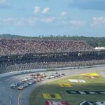 NASCAR Cup Series cars racing in a tight pack at Talladega Superspeedway with a full grandstand.