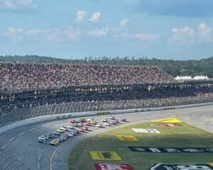 NASCAR Cup Series cars racing in a tight pack at Talladega Superspeedway with a full grandstand.