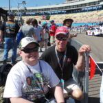 Two NASCAR fans smiling along pit road at Phoenix Raceway.