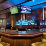 Modern hotel bar with glowing blue backlighting and flat-screen TVs at Embassy Suites Phoenix–Tempe.