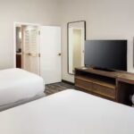 Embassy Suites Orlando North bedroom with two beds, flat-screen TV, and modern furnishings.