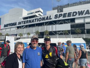 Three RaceAway guests pose outside Daytona International Speedway before the 2026 Daytona 500, with the grandstands behind them.