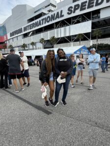 Two RaceAway guests pose for a photo outside Daytona International Speedway during the Daytona 500 weekend, with the grandstand signage behind them.