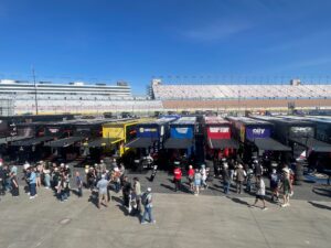NASCAR Cup Series team haulers line the garage area at Las Vegas Motor Speedway during a race weekend as fans walk through the infield.