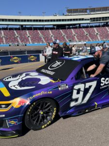 The No. 97 NASCAR Cup Series car sits on pit road at Phoenix Raceway during the 2026 Straight Talk Wireless 500 as guests gather nearby.