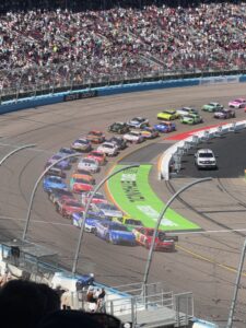A packed field of NASCAR Cup Series cars races through a turn at Phoenix Raceway during the 2026 Straight Talk Wireless 500.