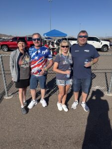 Four RaceAway guests pose for a photo outside Phoenix Raceway during the 2026 Straight Talk Wireless 500 with tailgating and desert mountains in the background.