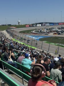 NASCAR Cup Series cars race through the turn at Kansas Speedway during the 2026 AdventHealth 400 as fans watch from the grandstands.