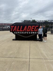 Two RaceAway guests pose in front of the Talladega Superspeedway sign near the garage entrance.