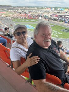 Two RaceAway guests pose from the upper grandstands at Charlotte Motor Speedway during the 2026 Coca-Cola 600, with the frontstretch and pre-race scene below.