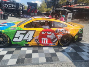 A RaceAway guest sits inside a colorful No. 54 M&M’s NASCAR display car at Bristol Motor Speedway during the 2026 Bass Pro Shops Night Race weekend.