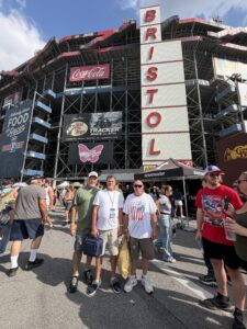 Three RaceAway guests pose beneath the towering Bristol Motor Speedway grandstands during the 2026 Bass Pro Shops Night Race weekend.