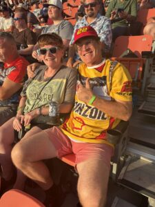 Two RaceAway guests smile from the grandstands at Bristol Motor Speedway during the 2026 Bass Pro Shops Night Race, including a fan wearing Joey Logano gear.