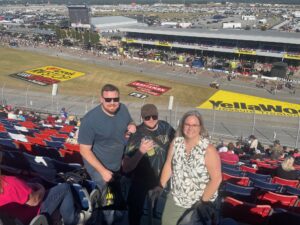 Three RaceAway guests pose in the Talladega Superspeedway grandstands overlooking pit road during the October 2026 YellaWood 500 weekend.