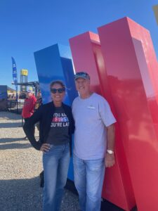 Two RaceAway guests pose beside a colorful NASCAR display in the fan area at Talladega Superspeedway during the October 2026 YellaWood 500 weekend.