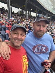 Two RaceAway guests pose together in the Phoenix Raceway grandstands during the 2026 Freeway Insurance 500, with a packed crowd behind them.
