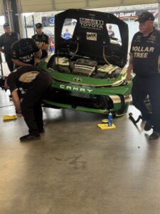 Legacy Motor Club crew members work on a green Dollar Tree Toyota Camry inside the Phoenix Raceway garage during the 2026 Freeway Insurance 500 weekend.